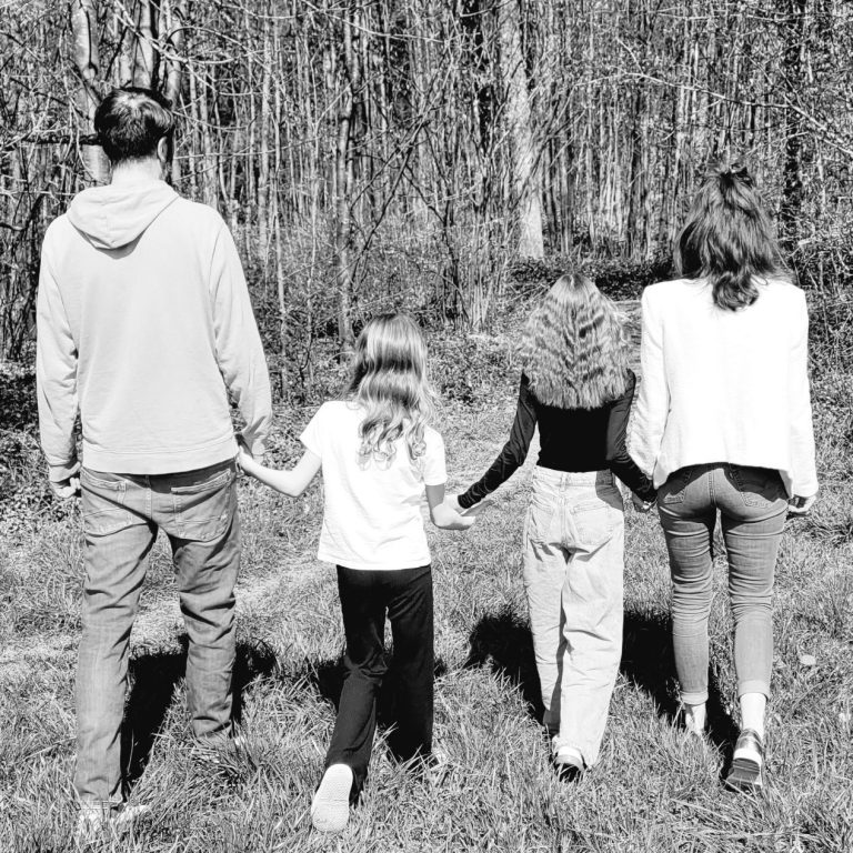 Familientherapie Eltern mit zwei Kindern laufen einen Waldweg entlang in einem Schwarzweiß-Foto