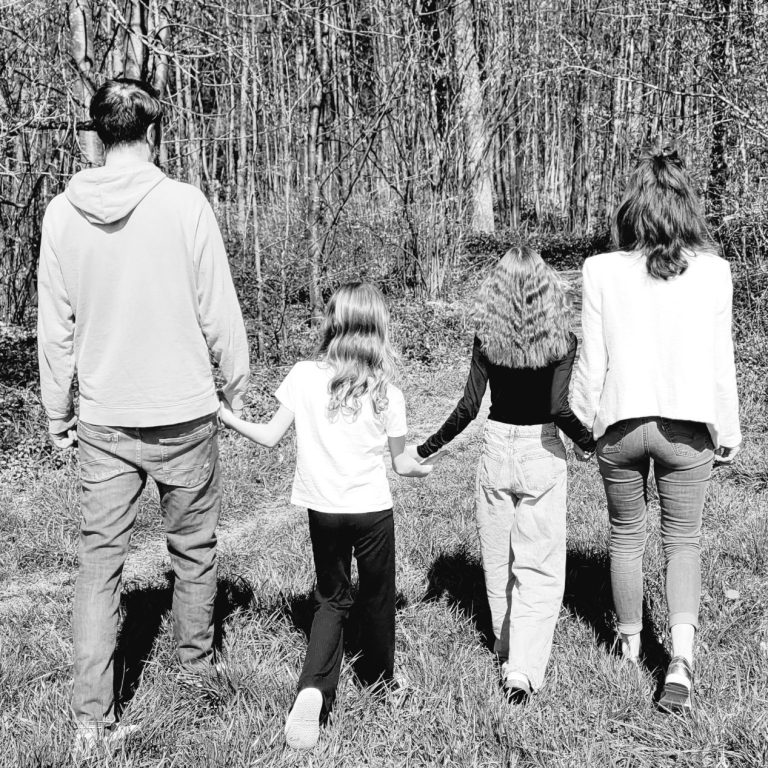 Eltern-Coaching Eine Familie läuft Hand in Hand auf einen Wald zu in einem Schwarzweiß-Foto