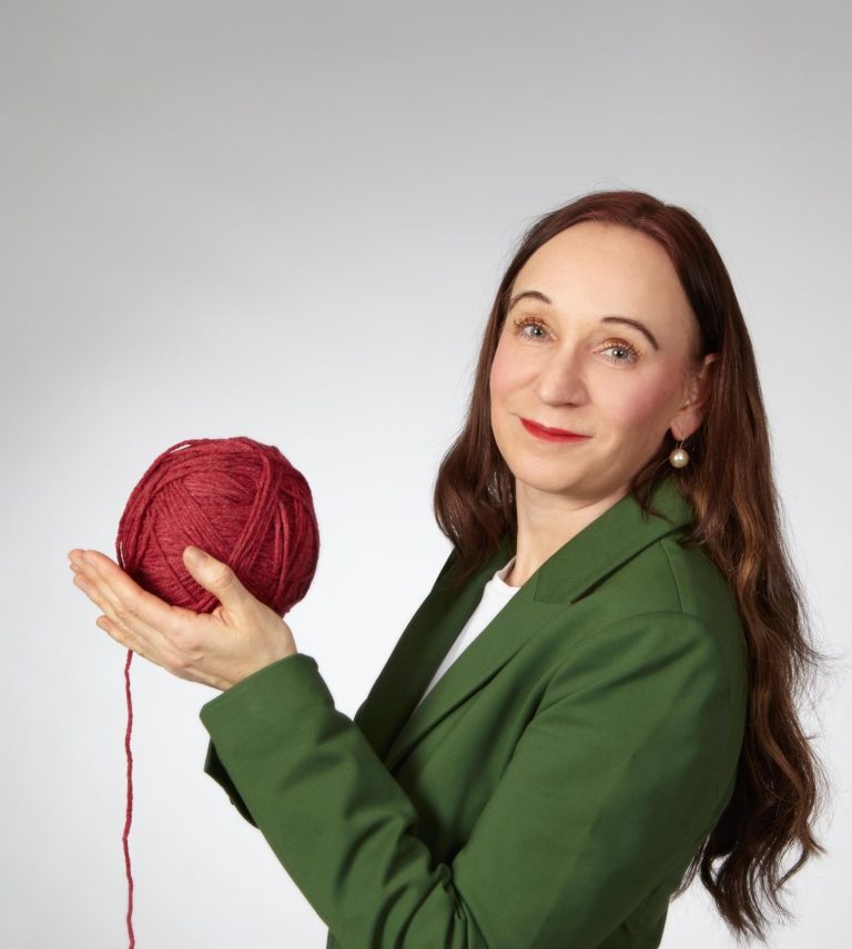Birgit Cyba - ELiB Birgit Cyba mit einem roten Wollknäuel in der Hand, von dem ein Faden nach unten hängt